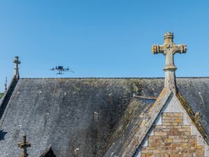 Photographie aérienne d'un drone de pulvérisation entrain de nettoyer la toiture en ardoise d'une église.